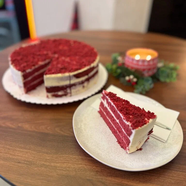 Kousek dortu Red Velvet s krémovým sýrem a celý dort v pozadí v nabídce kavárny GP Caffé